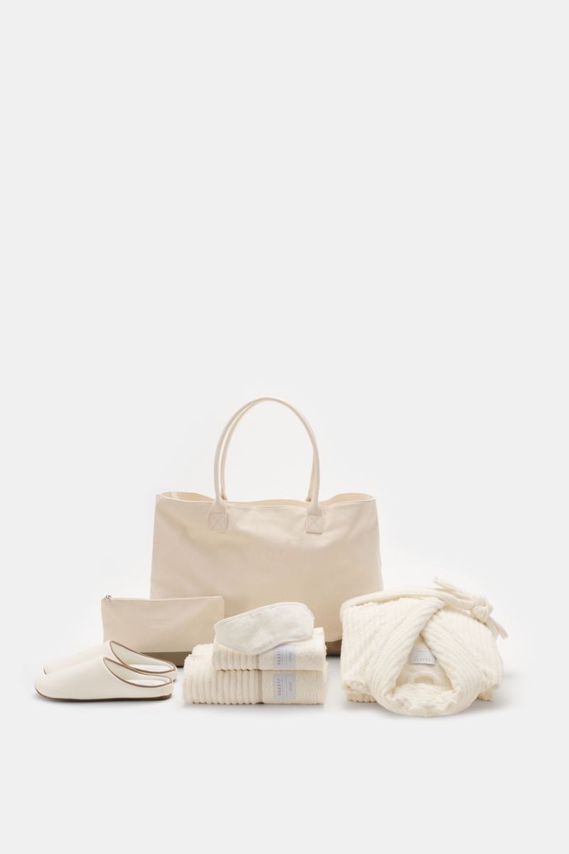 Front view of 04651/ A trip in a bag Reise-Set 'Voyage' creme/weiß featuring a large cream canvas shopper with sturdy handles, a folded bathrobe, hand towel, bath towel, zippered necessaire, indoor slippers, and a sleep mask, all neatly arranged for a sty