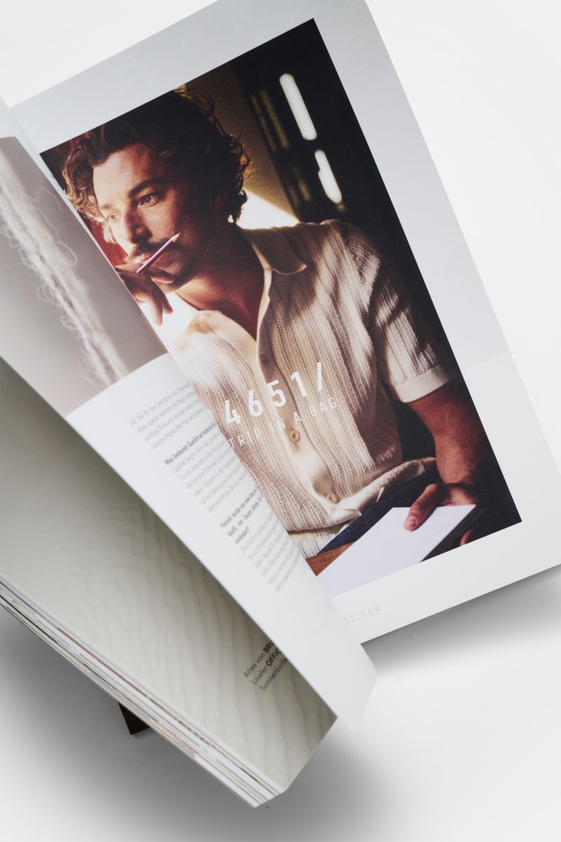 Close-up view from above of Edition EDITION Magazin Frühling 2026 open to a page showing a thoughtful man in a knitted shirt holding a pen to his lips, reflecting authenticity and elegance. Entdecken Sie Vol. 18 von EDITION – ein Magazin, das Mode, Rei