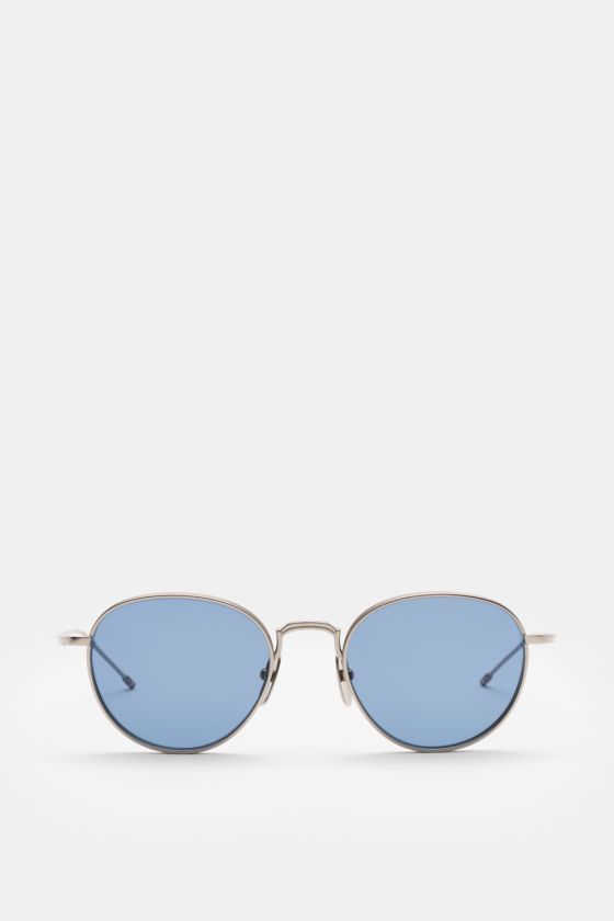 Thom Browne Sonnenbrille silbergrau, frontale Nahaufnahme, runde Form, tiefem Metallrahmen, blau getönte Gläser, Tricolore-Detail am Bügel, 100% UV-Schutz. Thom Browne Sonnenbrille silbergrau, frontale Nahaufnahme, runde Form, tiefem Metallrahmen, blau getönte Gläser, Tricolore-Detail am Bügel, 100% UV-Schutz.
