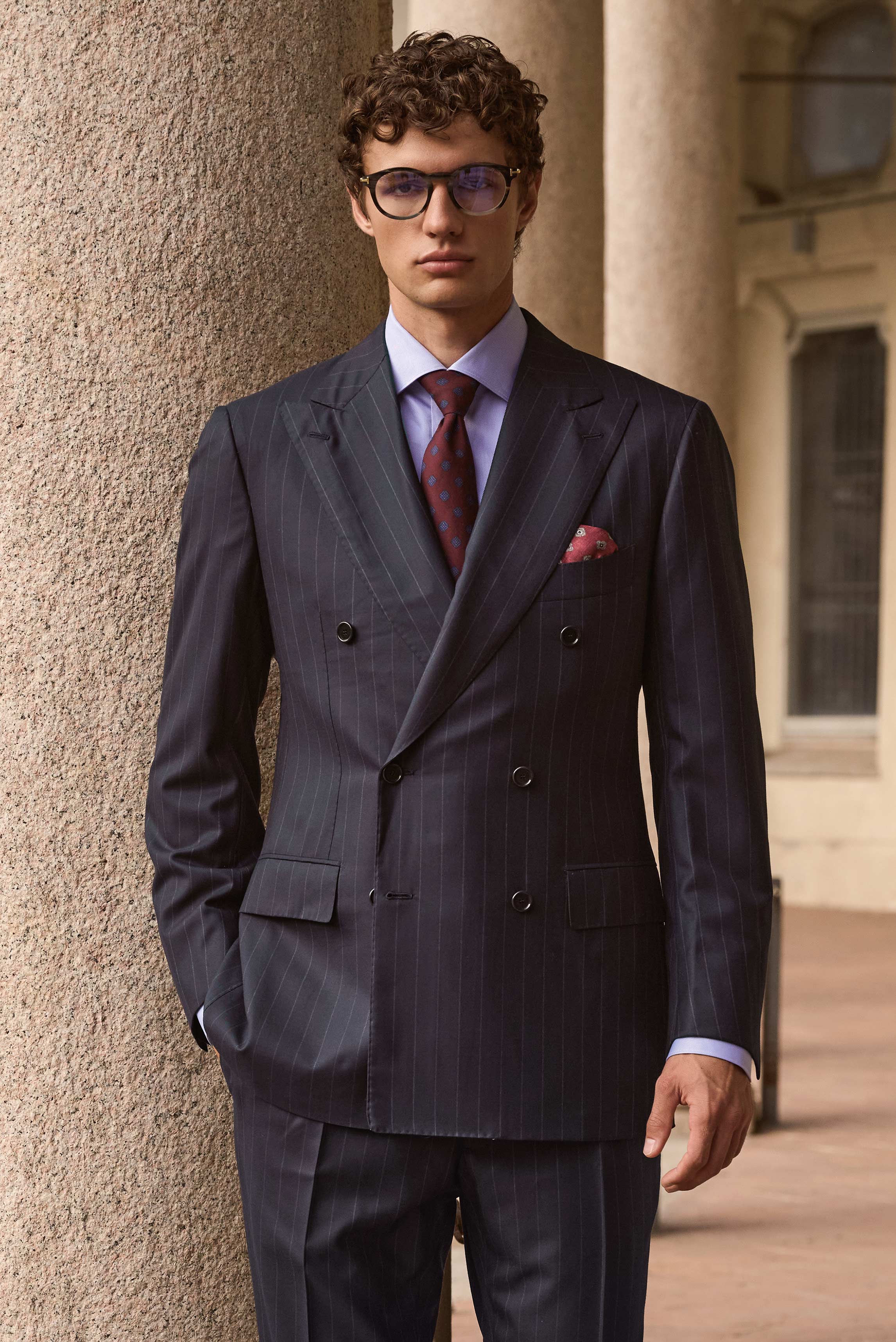 Front view of a model wearing a navy striped double-breasted suit from Cesare Attolini, light blue 'Nando' shark collar shirt from Borrelli, burgundy and blue 'Ventaglio' tie from Cesare Attolini, dark red and grey silk pocket square from Brunello Cucinel