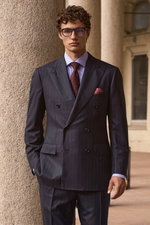 Front view of a model wearing a navy striped double-breasted suit from Cesare Attolini, light blue 'Nando' shark collar shirt from Borrelli, burgundy and blue 'Ventaglio' tie from Cesare Attolini, dark red and grey silk pocket square from Brunello Cucinel