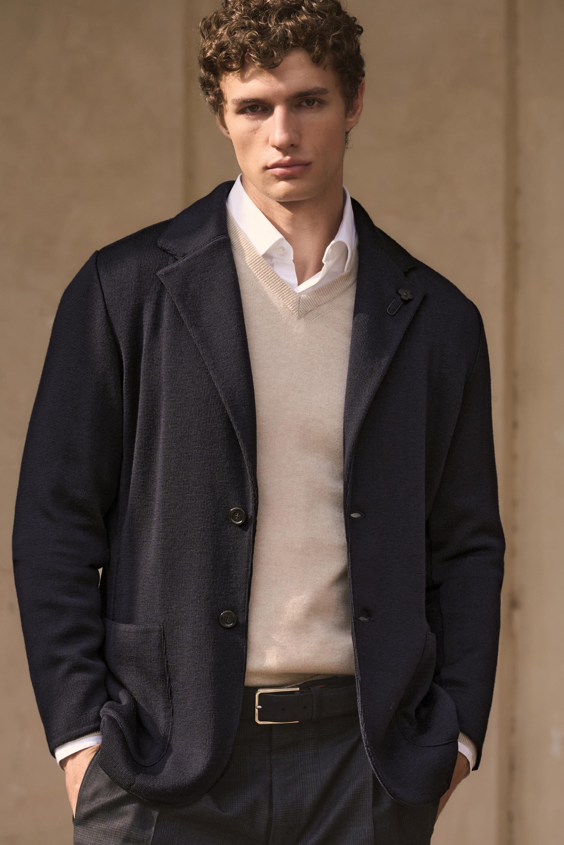 Porträtaufnahme eines Mannes frontal von oben bis zur Hüfte, das Modell trägt einen navyfarbenen Strickblazer von Lardini, kombiniert mit einem sandmelierten Cashmere V-Neck Pullover von Aida Barni, darunter ein weißes Business Hemd „Nando“ mit Haifisch-K