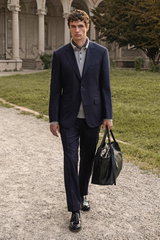 Shop by Look 12 Edition Vol. 19 front view of a model dressed in a navy striped Canali suit 'Giacca', grey cashmere polo by Fioroni, navy violet Brunello Cucinelli pocket square, black Church's 'Pembrey' loafers, carrying a black Serapian shopper bag, wal