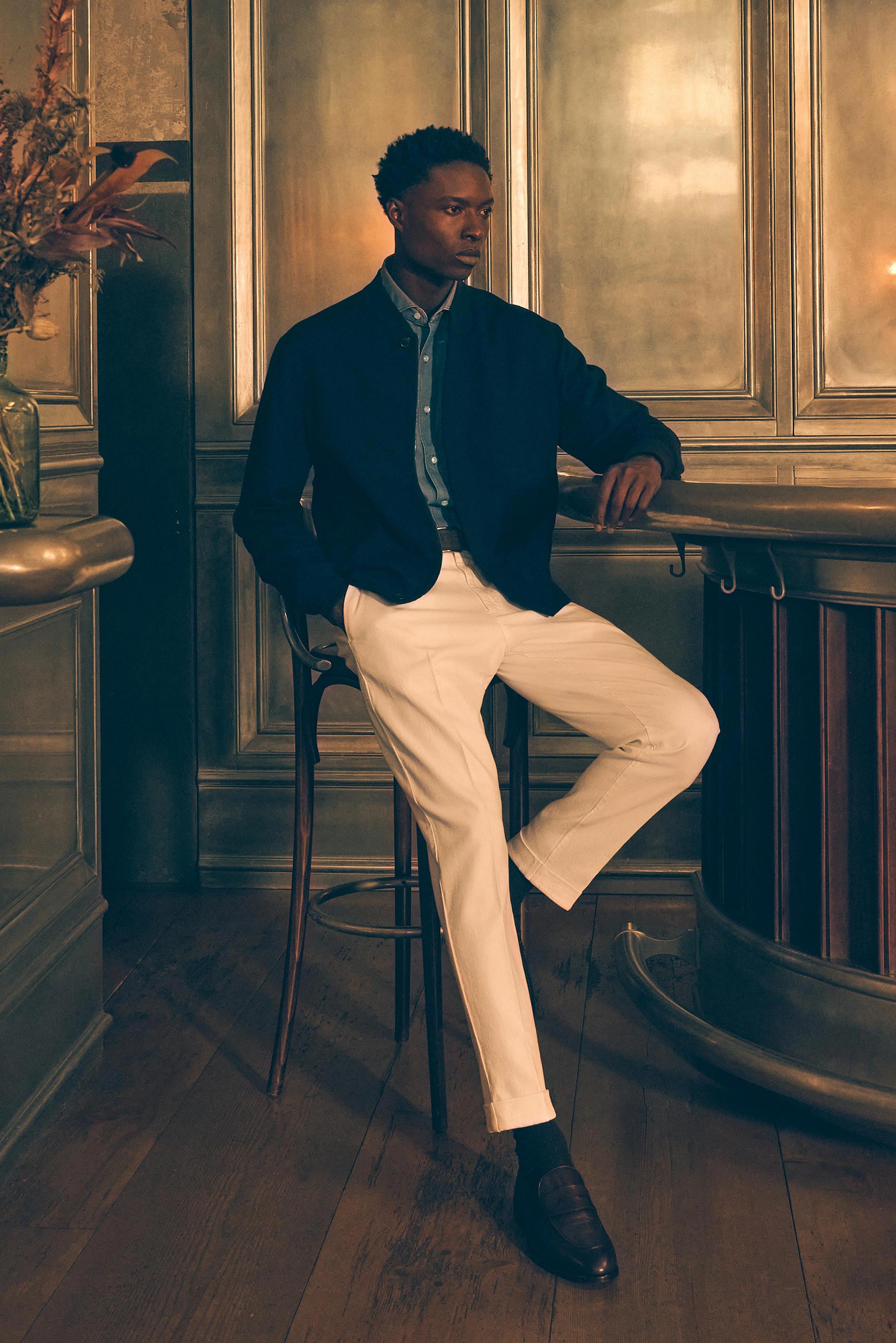 Shop by Look 13 Edition Vol. 19 shows a model seated in a side view, wearing a blue chambray shirt with shark collar by Finamore, white "The Rebel" pants from PT Torino, a dark brown Veneta Cinture belt, and dark brown "Moro" penny loafers by Henderson, b
