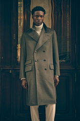Front view of a model in Shop by Look 16 Edition Vol. 19 wearing a sophisticated grey-green melange double-breasted Brunello Cucinelli coat with large buttons and pockets, a light grey melange and taupe patterned turtleneck sweater, and sand-colored cordu