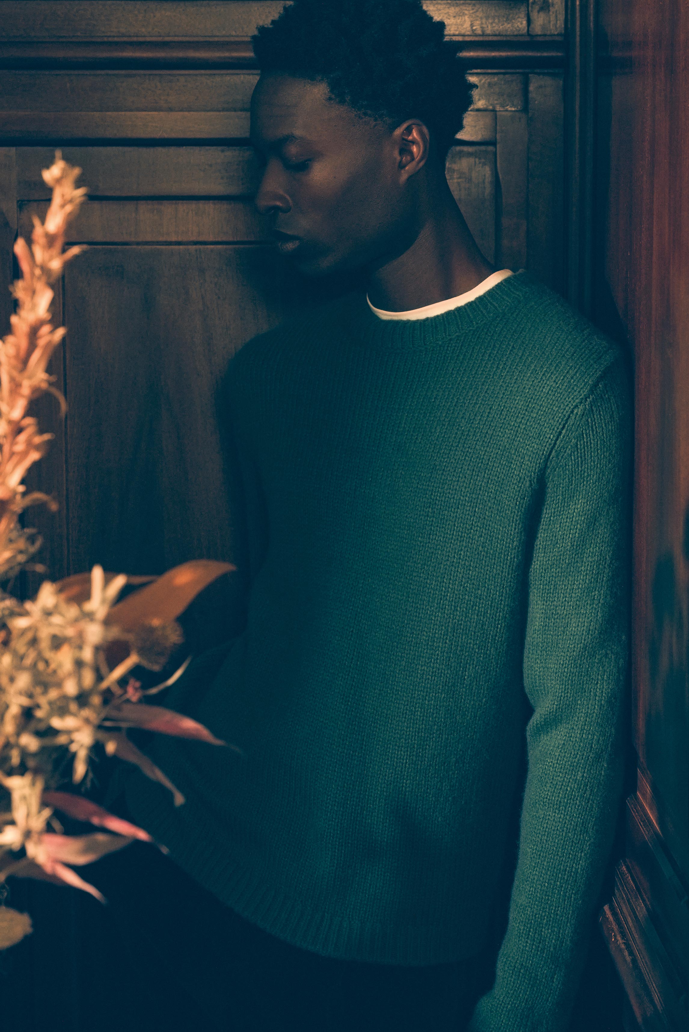 Model seitlich im Porträt vor Holzpaneelen, trägt grünen Cashmere-Seide Pullover 'Felton' von Iris von Arnim, weißes Longsleeve 'Alberts' von Kiefermann, Shop by Look 18 Edition Vol. 19.