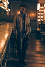 Front view of a model in an elegant interior, dressed in a dark brown and beige patterned down blouson from Montecore over a dark brown knit shirt by Allude, a grey brown melange cashmere crew neck sweater 'Duvet' from Fioroni, grey-brown melange wool pan