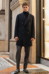 Front view of a model wearing a navy short coat from Mandelli over a navy fine knit turtleneck sweater from FTC, paired with grey melange jogpants 'Chiaia' from Marco Pescarolo and black leather shoes. The sophisticated and elegant look combines tailored 