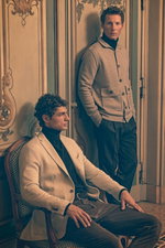 Two men in a vintage room captured from a slight side angle; standing model wears a beige melange knit cardigan from Allude over a dark green cashmere turtleneck by B.F. Knitwear, dark grey melange wool "Carrot Fit" trousers from PT Torino, and a grey-bro
