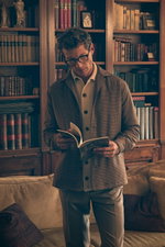 Shop by Look 36 Edition Vol. 19 front view of a man reading, wearing a light brown, bordeaux, and navy checkered 'Aabba' jacket by Doppiaa, cream Filippo de Laurentiis cardigan buttoned up, cream 'Herrick' chinos from GTA, and dark-framed glasses, in a co