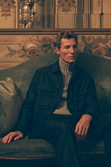 Man seated on a green vintage sofa in ornate room, wearing navy overshirt from Incotex over grey melange half-zip jumper from Allude with navy wool pants by Incotex, photographed from a frontal perspective; Shop by Look 38 Edition Vol. 19 showcases rich n