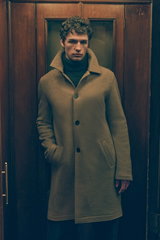 Front view of a male model wearing a light brown cashmere short coat from Lunaria Cashmere with high collar and button closure, dark brown cashmere turtleneck sweater from FTC underneath, showcasing a sophisticated warm look in earthy tones, Shop by Look 