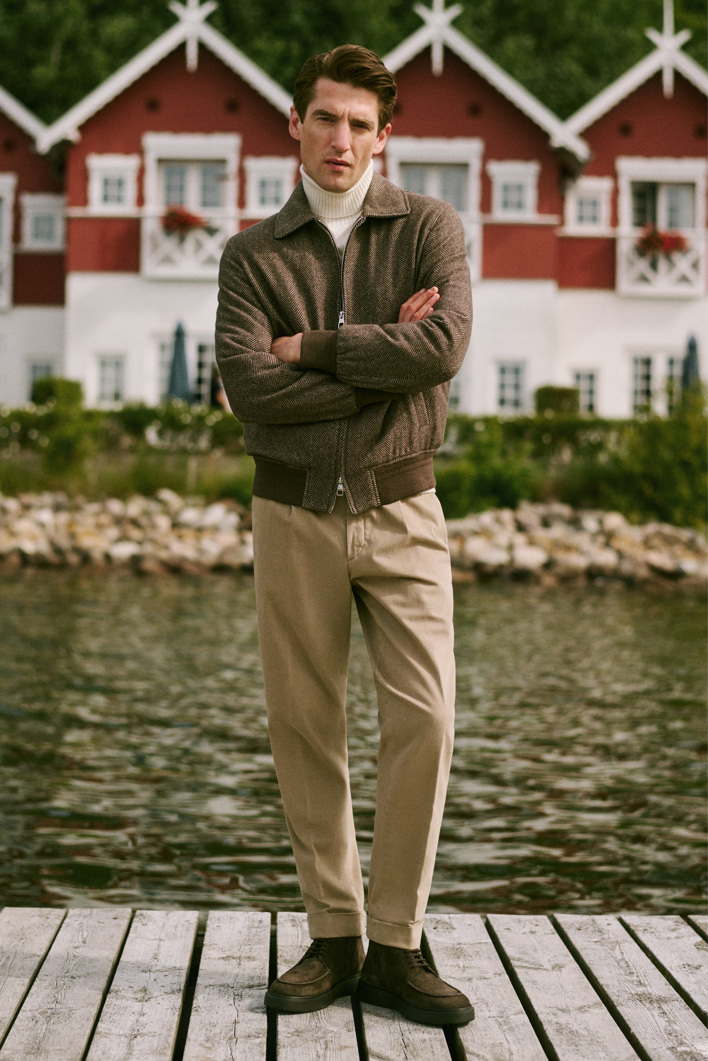 Mann frontal stehend am Steg, trägt weißen Rollkragenpullover, braune Jacke, beige Hose, Wildleder-Stiefel, Shop by Look 05 HW 2026.