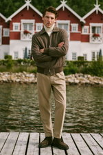 Mann frontal stehend am Steg, trägt weißen Rollkragenpullover, braune Jacke, beige Hose, Wildleder-Stiefel, Shop by Look 05 HW 2026.