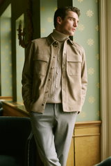 Shop by Look 09 HW 2026 shows a side-front view of a model wearing a beige suede Agnona overshirt with button-down front and flap pockets, a light beige cable-knit turtleneck sweater underneath, and light gray trousers, creating a sophisticated, elegant o