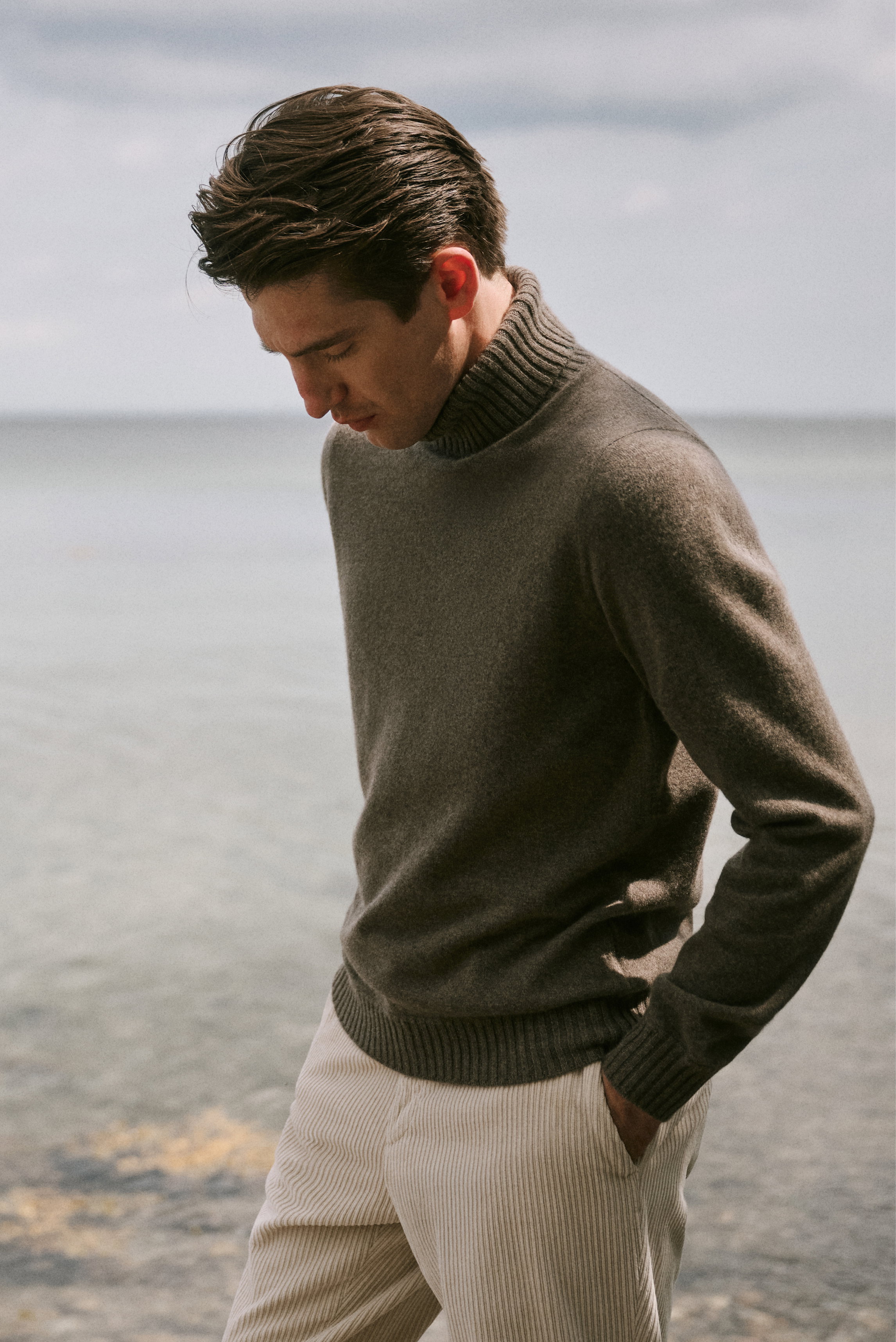 Shop by Look 29 HW 2026 shows a side view of a model wearing a grey-brown mélange cashmere turtleneck sweater "Duvet" from Fioroni with ribbed texture, paired with sand-colored corduroy "Davide" pants from GTA featuring vertical ridges.