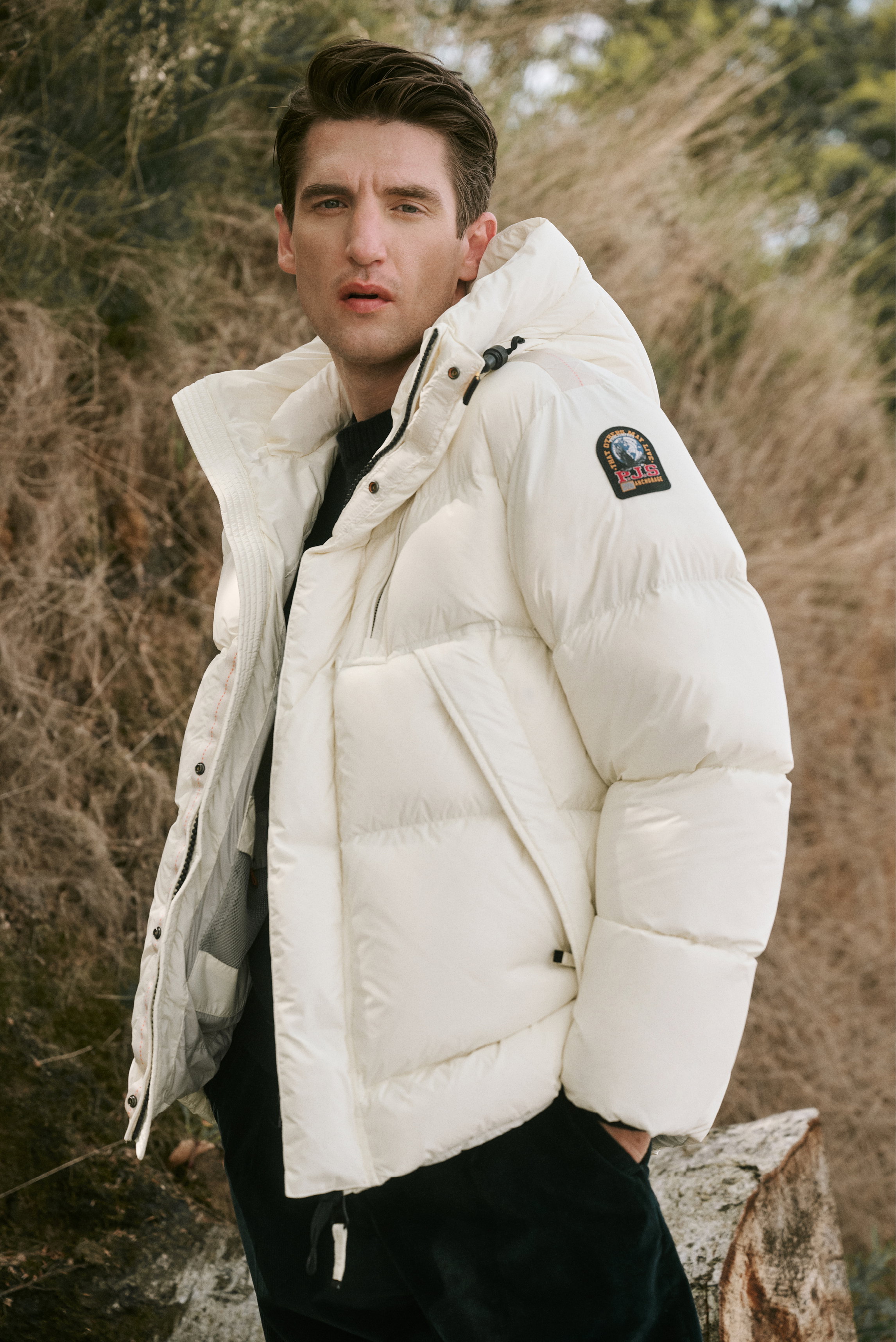 Front view of a male model outdoors wearing a cream puffer jacket with sleeve patch, navy 'Edmond' crew neck sweater by A.P.C., navy 'Rebel Fit' corduroy pants by PT Torino, and dark brown 'Frame' lace-up boots by Officine Creative in Shop by Look 31 HW 2