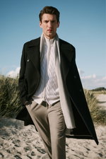 Männliches Modell frontal fotografiert, trägt schwarzen Mantel von Barena Venezia, weißen grob gestrickten Pullover, graue Hose von Closed – Shop by Look 41 HW 2026.