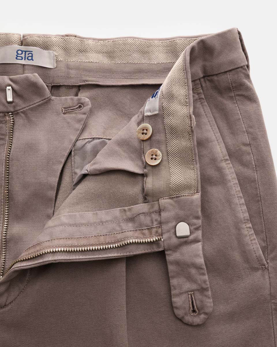 Close-up of beige pants with partially open zipper, two buttons, and a small metal clasp on the waistband, showing inner fabric.
