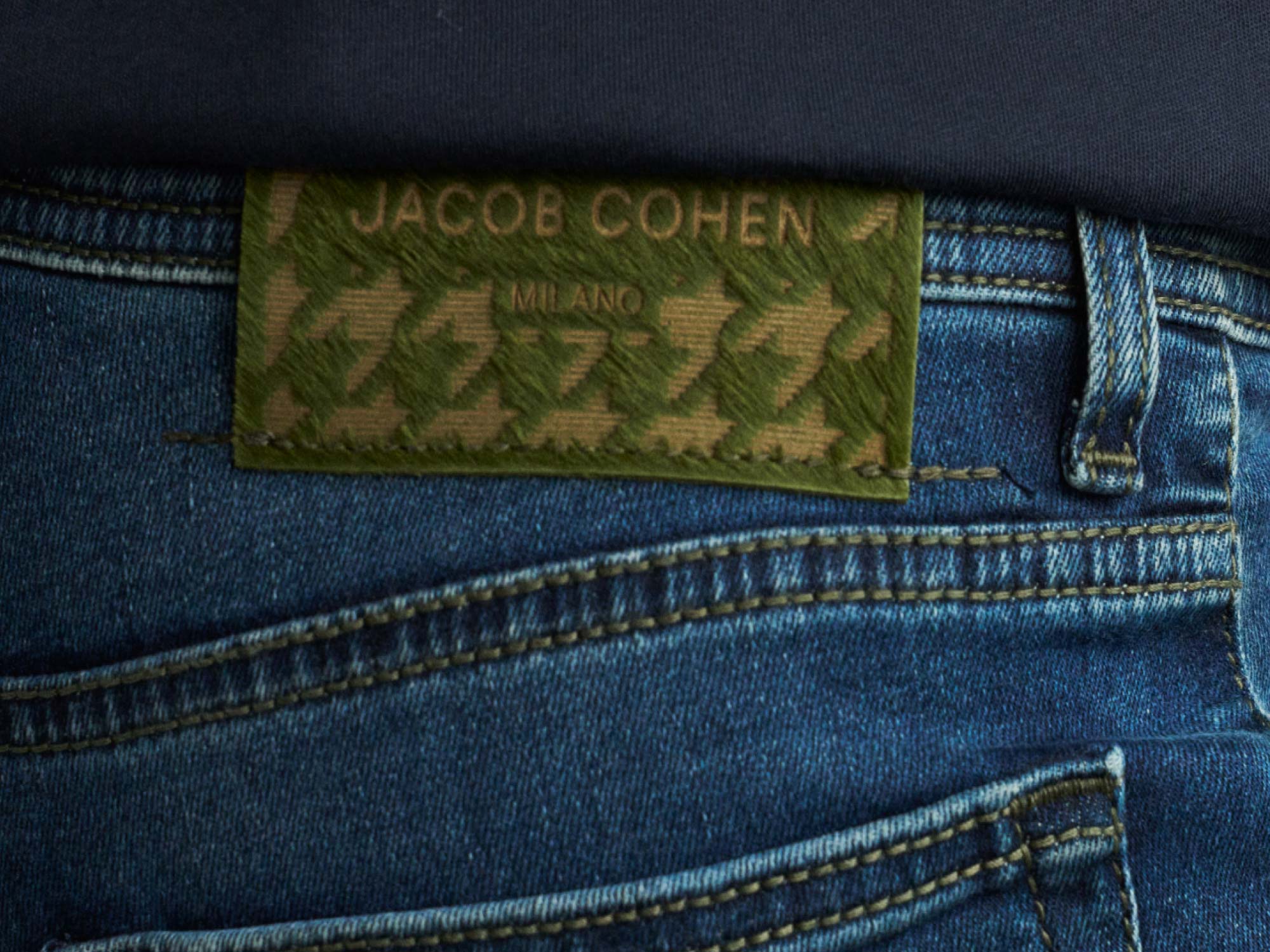 Jeansbund mit grünem Lederetikett "Jacob Cohen Milano" und blauem Jeansstoff mit sichtbarer Naht, schwarzes Oberteil.