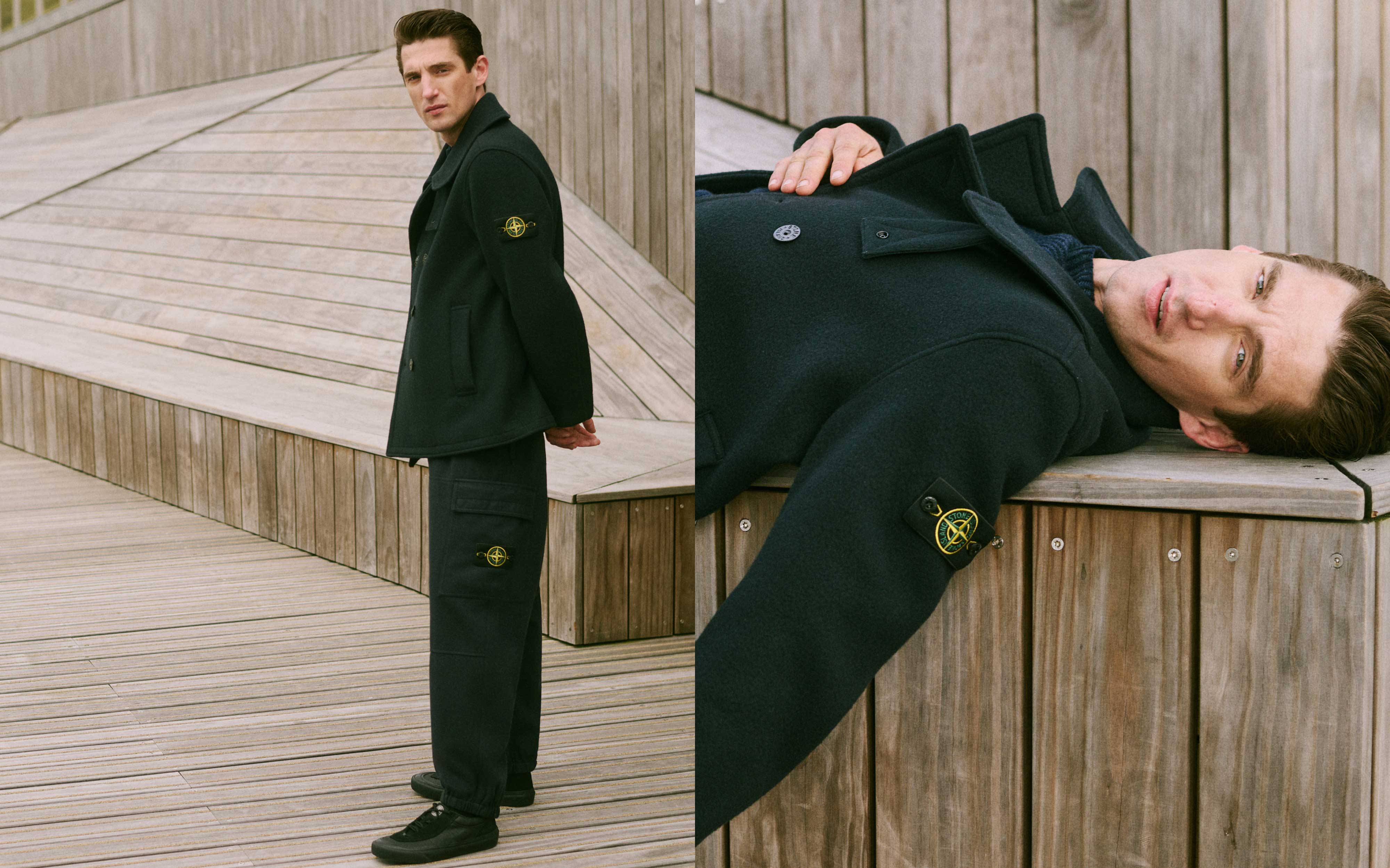 Mann in schwarzem Stone Island Mantel und Hose posiert stehend und liegend auf Holzterrasse mit moderner Architektur im Hintergrund.