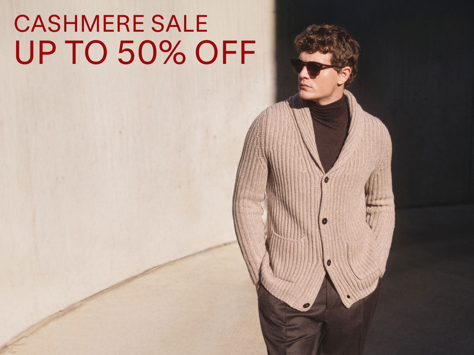 Mann mit Sonnenbrille trägt beigen grob gestrickten Cashmere-Cardigan, daneben roter Text „Cashmere Sale up to 50% off“.