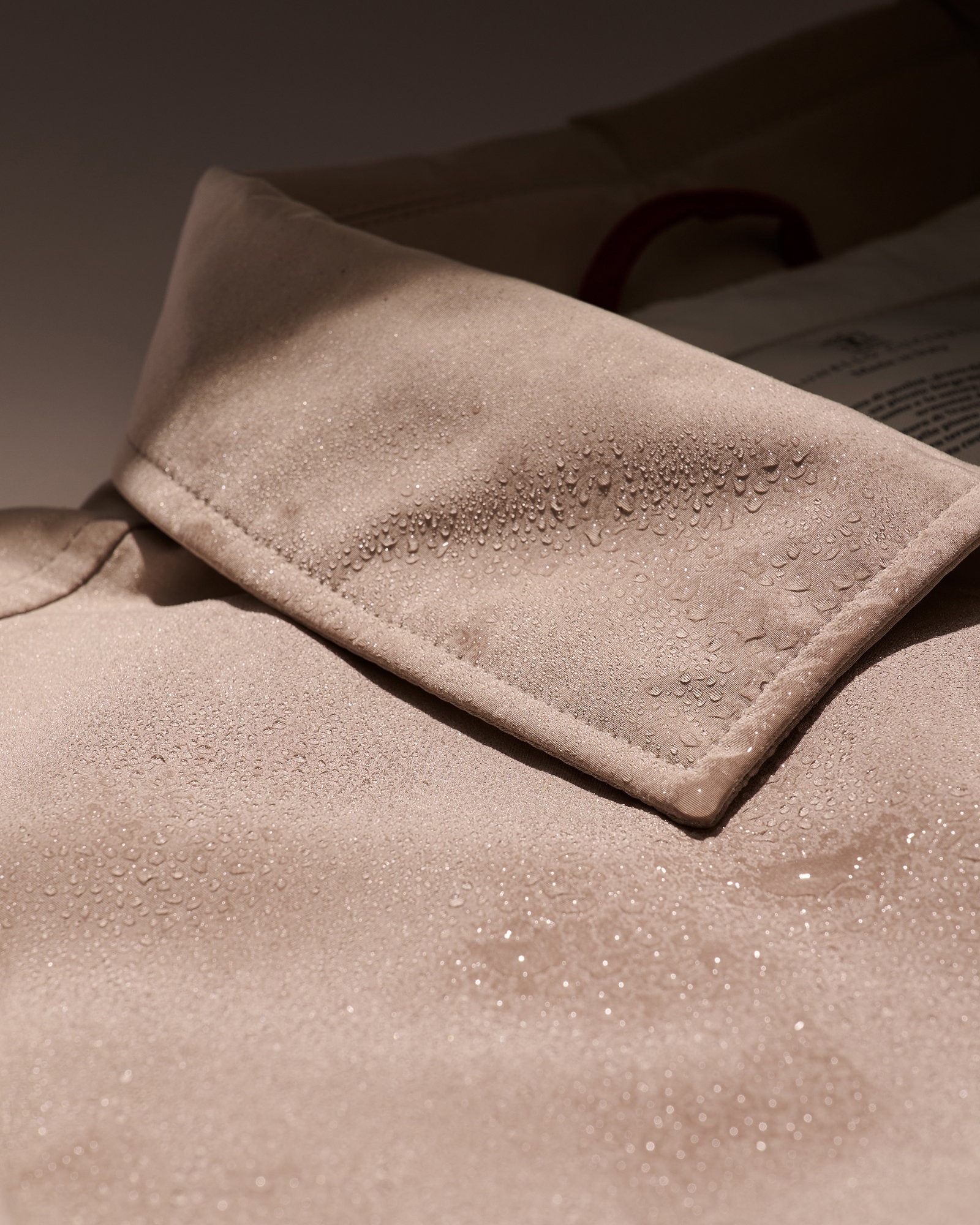 Beiger Kragen einer Herrenjacke mit vielen Regentropfen, die an der wasserabweisenden Oberfläche abperlen.