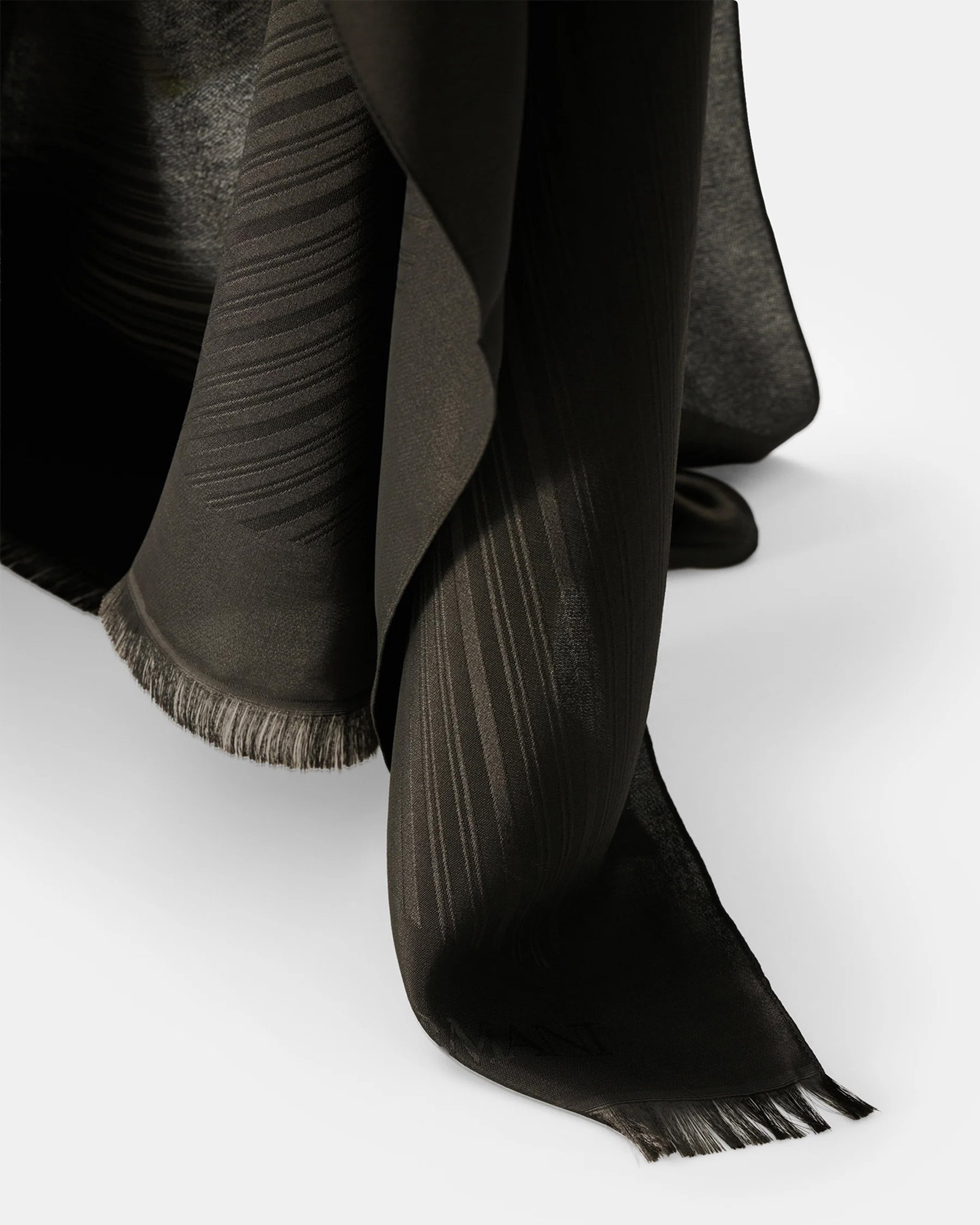 Schwarzes Polyester-Tuch mit feinem Streifenmuster und breitem Fransensaum, locker hängend vor hellem Hintergrund.