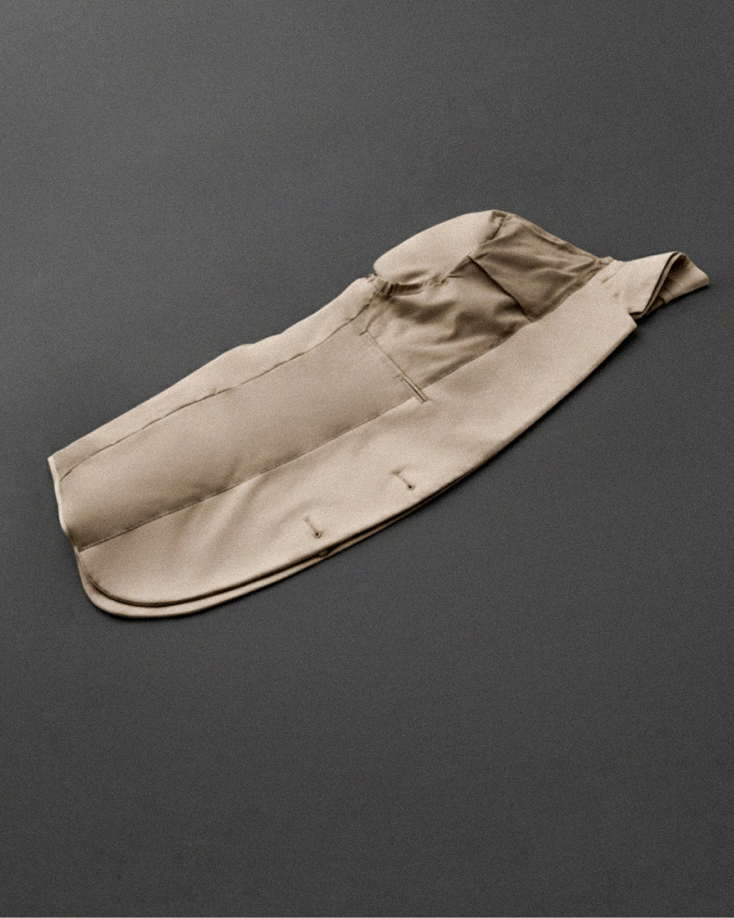 Gefaltetes beige Herren-Sakko, Innenseite nach außen zeigend, mit sichtbaren Nähten und Taschen auf dunklem Hintergrund.