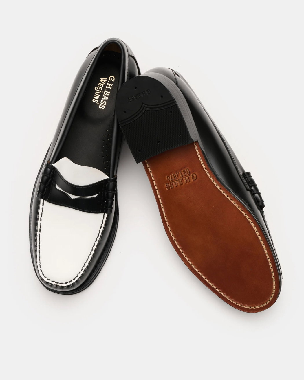 Schwarze und weiße Herren-Loafer aus Leder, eine liegend mit sichtbarer brauner Ledersohle, auf weißem Hintergrund.