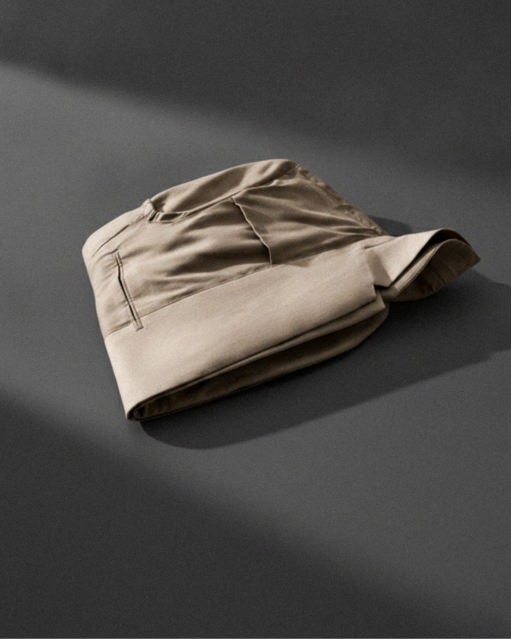 Beige Herren-Sakko-Innenseite mehrmals gefaltet auf dunklem, schattiertem Untergrund liegend, Detailaufnahme.