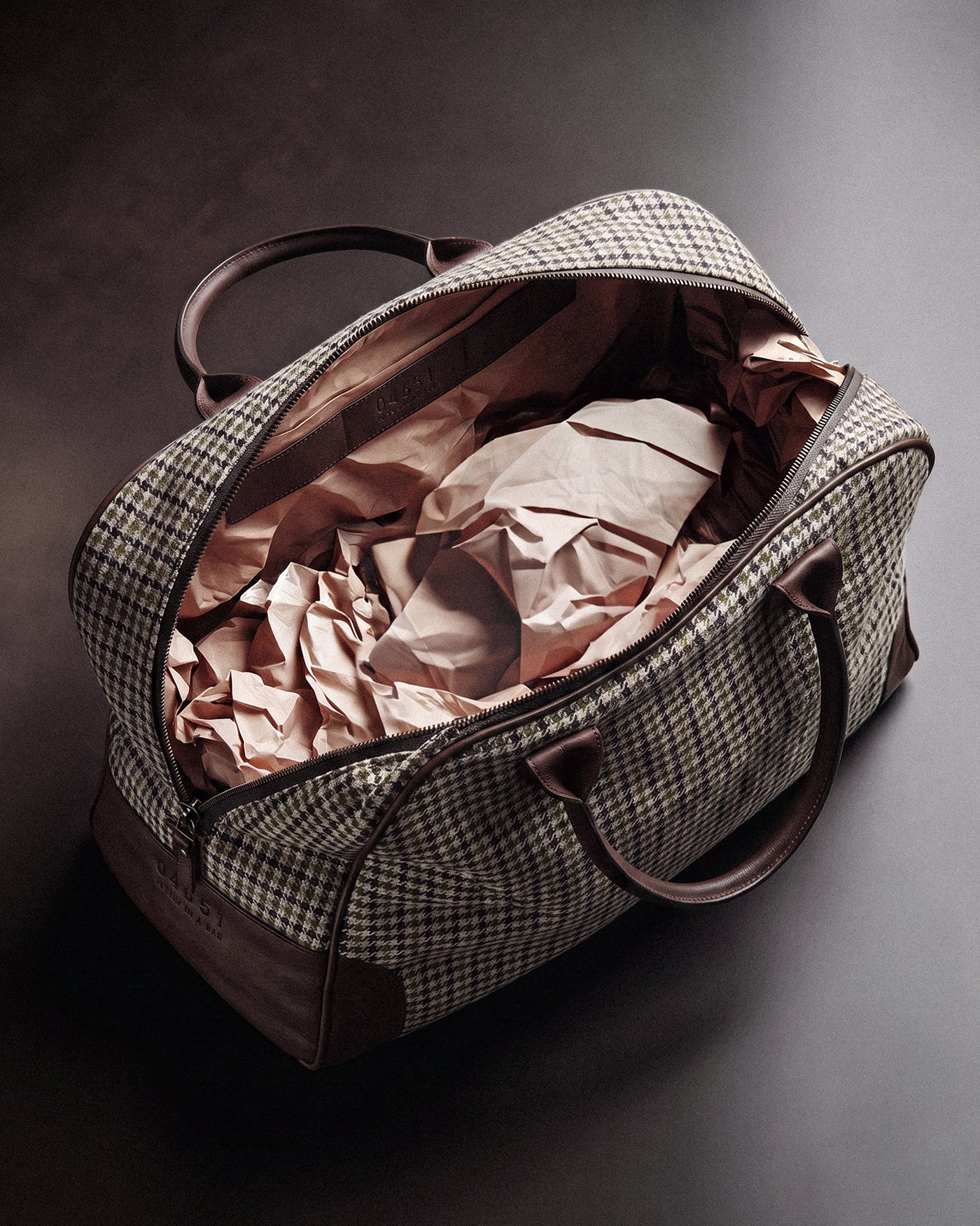 Offener Weekender-Tasche in braun-beigem Hahnentritt-Muster mit braunen Ledergriffen, innen mit zerknülltem Papier ausgepolstert.